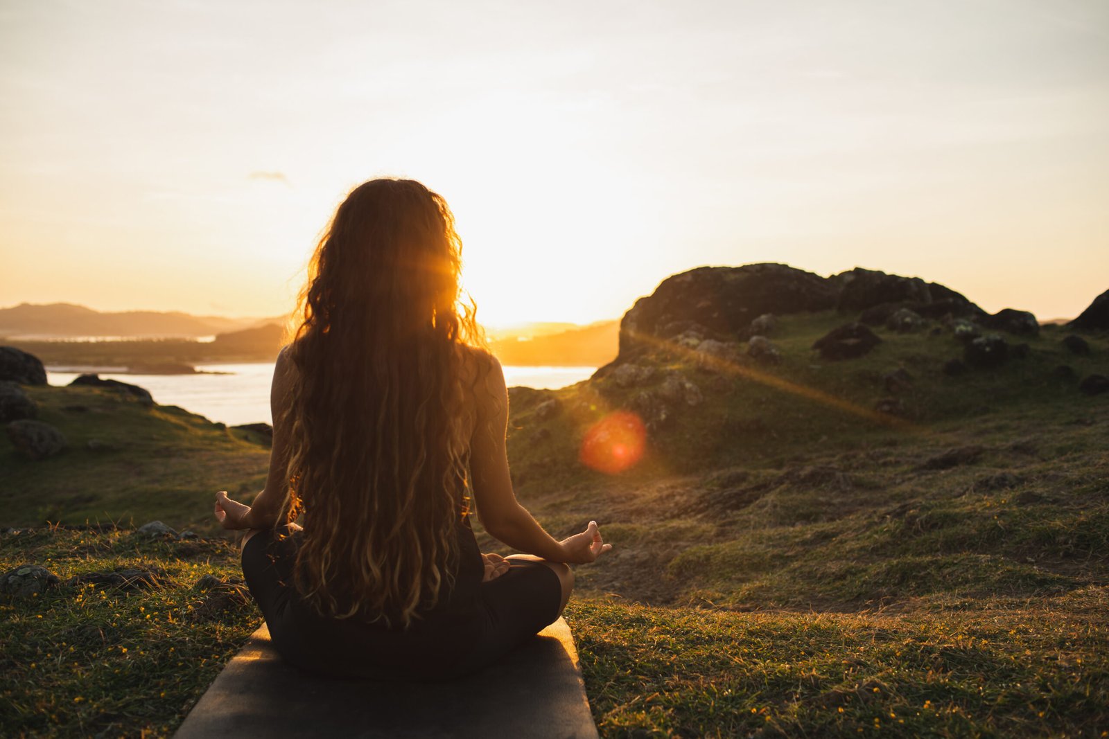 woman meditating yoga alone at sunrise mountains. view from behind